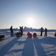 A group of people with their pulks in a polar landscape with the sun going down