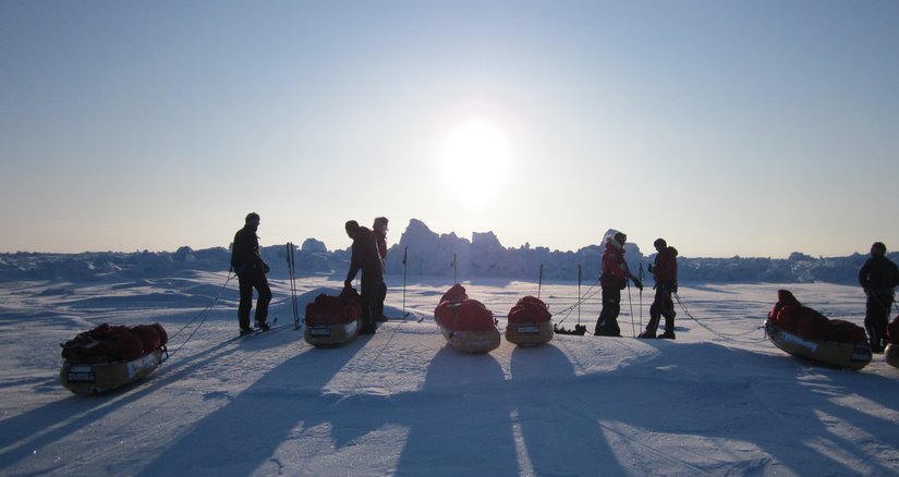 A group of people with their pulks in a polar landscape with the sun going down