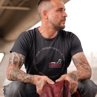 A man modelling a WWTW branded black T-shirt with a circle of words around the logo where letters are highlighted in red to spell veteran