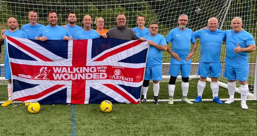 A team of footballers from Glasgow holding a WWTW branded Union Jack in front of goal posts